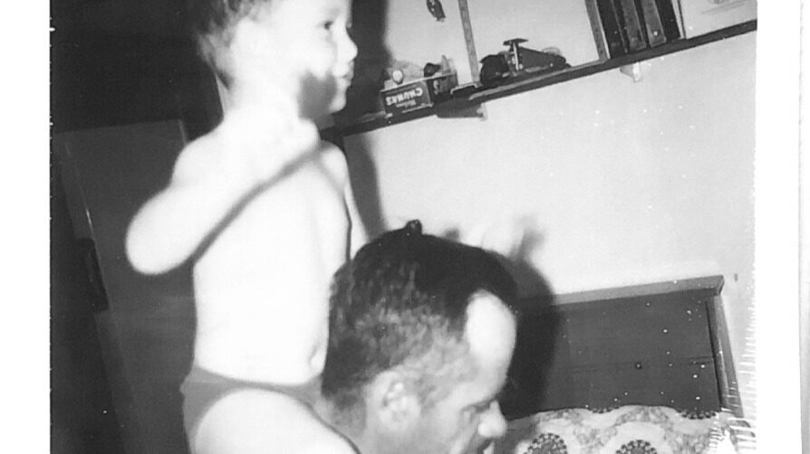 Vintage black-and-white photo of a small child standing on a couch beside a seated man — an intergenerational motif